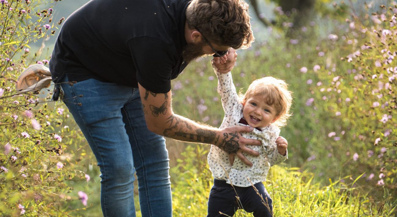 junger Vater führt sein Kleinkind an der Hand bei den ersten eigenen Schritten